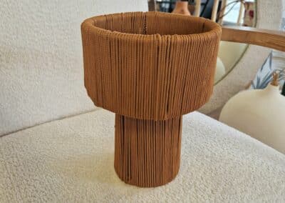 Vous&G agence immobilière Un vase brun, texturé et à large bord est posé sur une chaise rembourrée de couleur claire, avec une partie d'un miroir et d'autres objets de décoration visibles à l'arrière-plan.